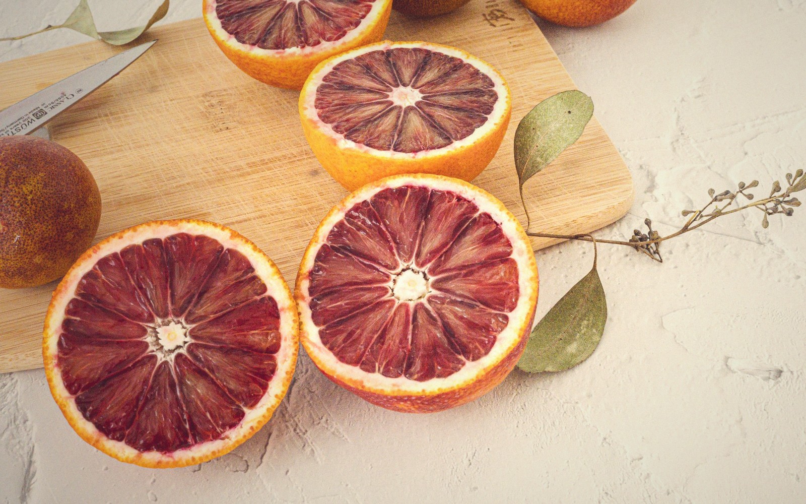 Halved blood oranges, dark board — the sharp lift.